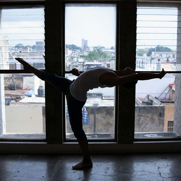 Silhouette of a person in a dynamic yoga stretch against a light background.